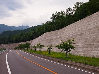 道路に沿って長く奥へと続いている国道122号沿いの原堆積場擁壁の写真