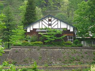 木造平屋・切妻屋根で、周りを緑の木々に囲まれている本山小学校講堂の外観写真