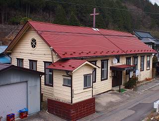 外壁がクリーム色で、赤い三角屋根をした屋根の上に十字架が設置されている足尾キリスト教会の外観写真