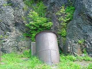 間藤水力発電所跡にある岩壁横の地面から出ている水圧管の一部の写真