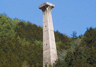 緑の木々が生えている山の斜面に建っている四角柱の塔で、上にいくにつれて柱が少し細くなっている有越鉄索塔の写真