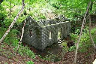 緑の木々に囲まれた中に建っている、石造りで屋根が無く外壁だけが残っている宇都野火薬庫跡の写真