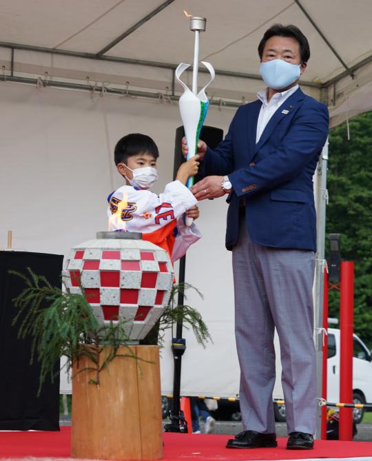 炬火の前でトーチを一緒に持つ、大人と子供の写真