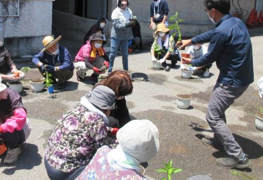 はじめてのプランター菜園に参加している人たちが中央の関係者の人の説明を聞いている写真