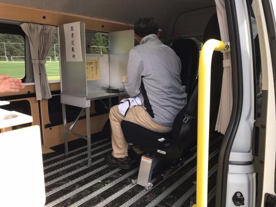マルチタスク車両内に設置されたシルバーの記載台の前に男性が座っている写真