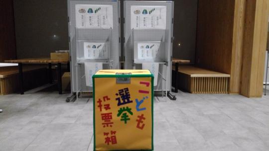 部屋の中央の黄色の箱に「こども選挙投票箱」と書かれた選挙時に使う投票箱がおかれた写真