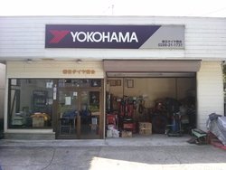 店舗上部に「YOKOHAMA」と書かれた看板があり、店舗内にはいろいろな工具等が並んでいる春日タイヤ商会の写真