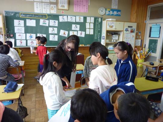 黒板にイラストが貼られた教室でグループごとに分かれ、先生が指導をしながら子ども達が話し合いをしている写真