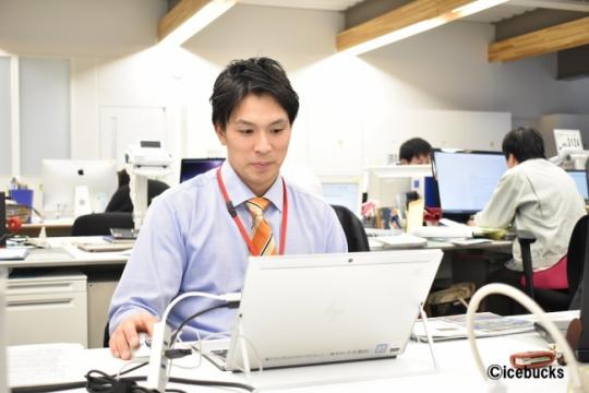 パソコンの前に座り右手にマウスを持ちデスクワークをしている岩本和真さんの写真