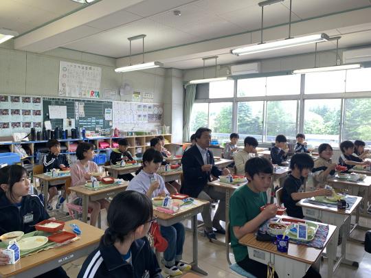 教室の真ん中の席に粉川市長が座り、今市小学校の子ども達と一緒に特別献立の給食を食べている写真