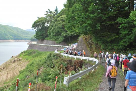 曲がりくねった道を背中にリュックを背負って歩いている、栗山ふるさとサマーウォーク参加者の方々の写真