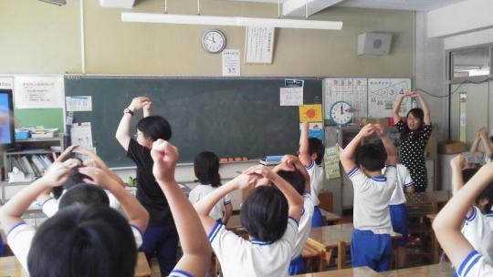 教室で2人の先生が指導しながら、子ども達が両手を上げ丸を作っている授業風景の写真