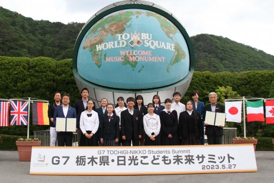 大きな地球儀の前で、G7栃木県・日光こども未来サミットに参加した中高校生たちと関係者の方々が一緒に記念撮影をしている写真
