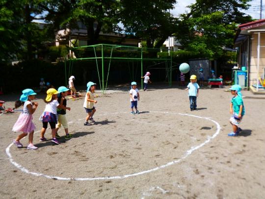 水色と黄色の帽子を被った子ども達が園庭でボール遊びをしている写真