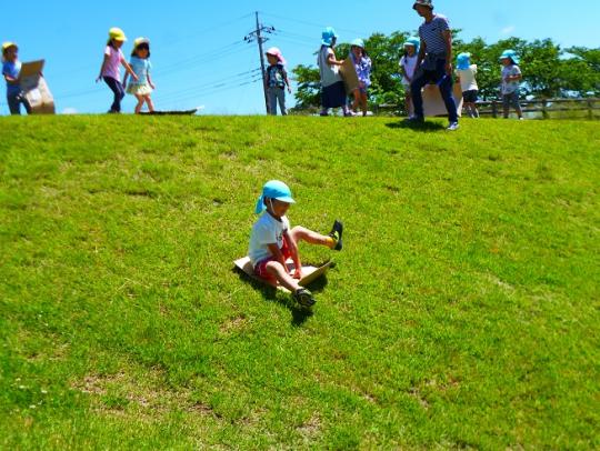 カラフルな帽子を被った子ども達が段ボールを使って芝滑りをしている写真