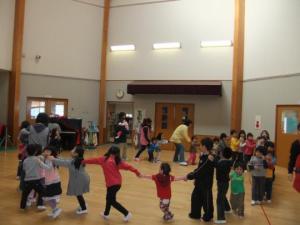教室で子ども達と先生が手を繋ぎ、輪になってダンスをしている写真