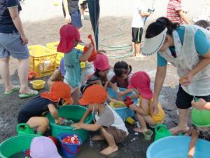 赤とオレンジの帽子を被った子ども達が裸足になって水遊びをしている写真
