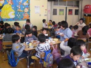 子ども達と先生がグループを作って席に座り、一緒に給食を食べている写真