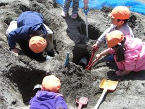 5人の子ども達が砂場で穴を掘って砂遊びをしている写真