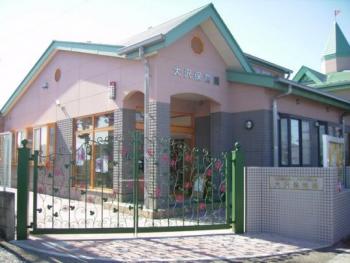 手前に緑の門、奥にピンクとグレーを基調とした大沢保育園園舎の写真