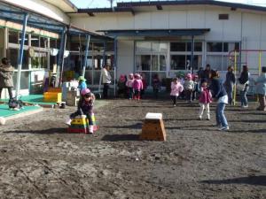 園庭でピンクの帽子を被った子ども達が順番に並び、跳び箱を飛んでいる写真