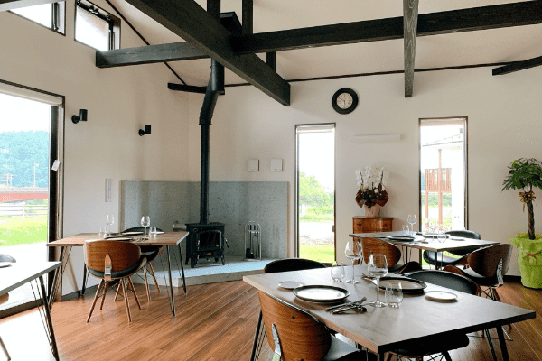 室内に4つの木製のテーブルが並べられ、大きな窓からは外が見えているオーベルジュ ブエナビスタの室内写真