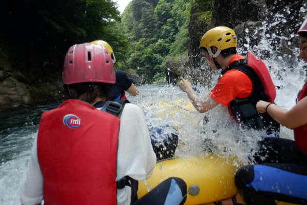 鬼怒川で参加者達が水しぶきをあげながらカヤックを楽しんでいる様子を後方から写した写真
