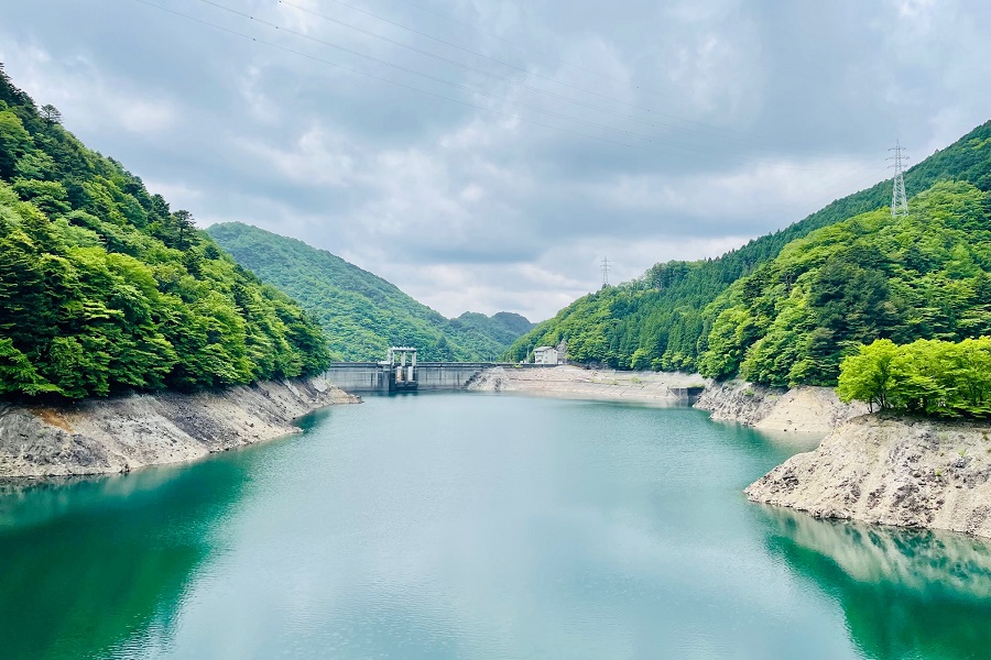 ゲートが閉じられ水面がエメラルドグリーンの今市ダム貯水池の写真