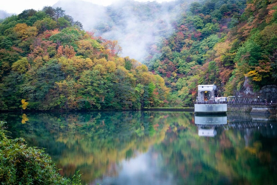 山々の紅葉が反射している幻想的な土呂部ダムの貯水池の写真