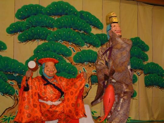 松が描かれた屏風の前で恵比須様と大黒様が舞っている写真