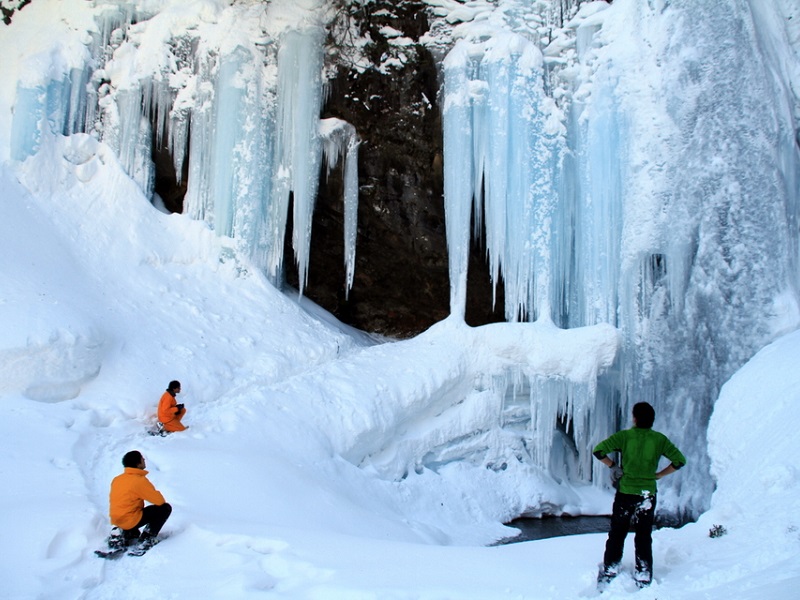 真っ白なパウダースノーの中スノーシューツアーの参加者3名が、前方にある雪で出来たつららを見上げている写真