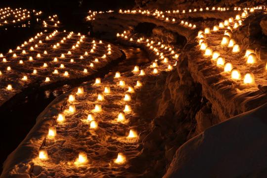 雪の積もった川の周りを小さなかまくらでできた灯篭が埋め尽くしている写真