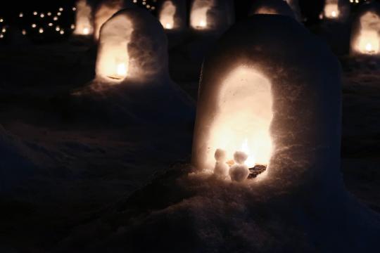 小さなかまくらの中に明かりをともして小さな雪だるまがふたつ飾られている様子の写真