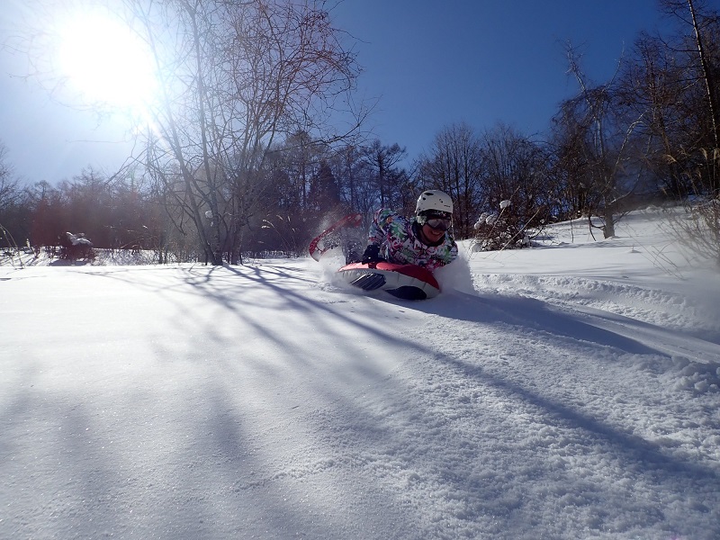 太陽の光が降り注ぐ中、雪の上でエアボードを楽しんでいる人の写真