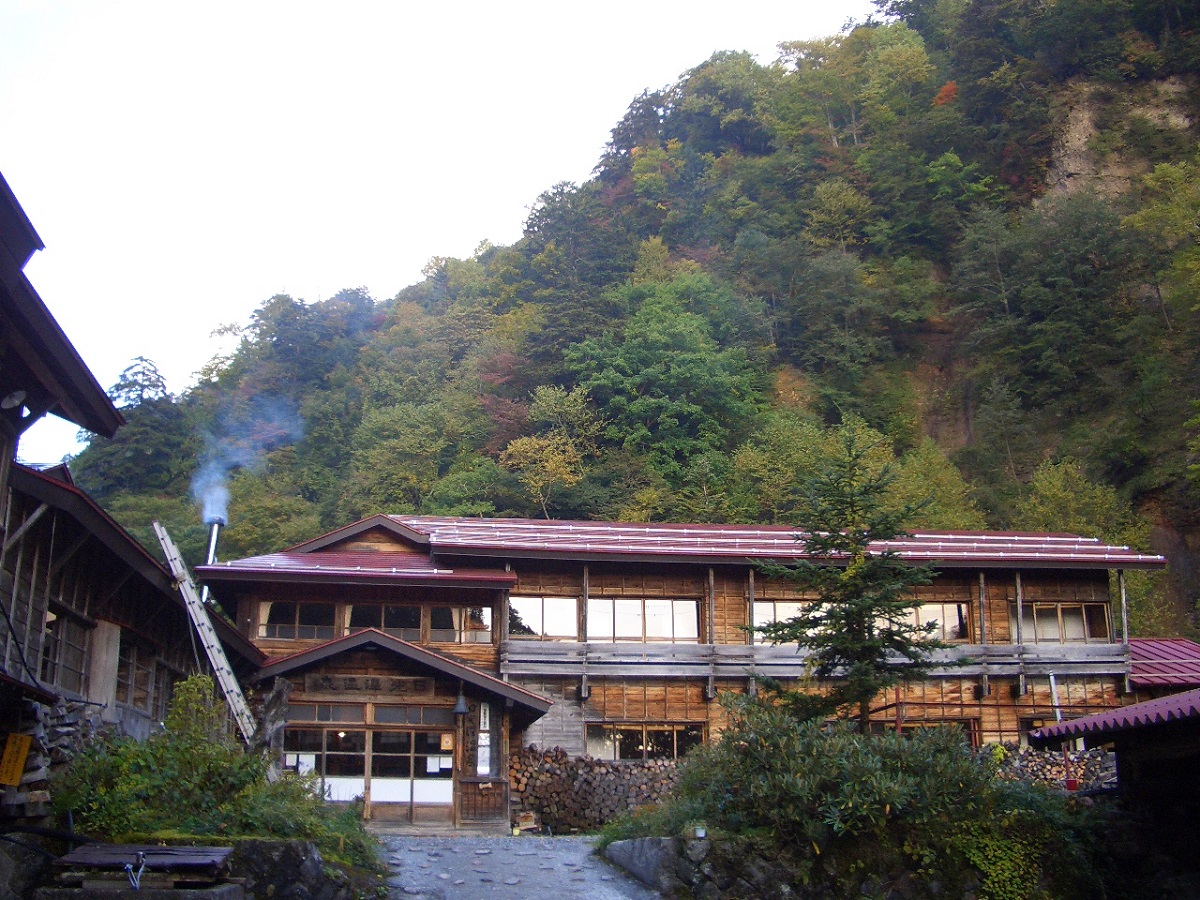 山の麓に建ち煙突から煙がでている日光澤温泉の外観写真