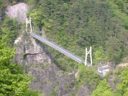 絶壁の間へ伸びた渡らっしゃい吊橋を山の斜面から写した写真