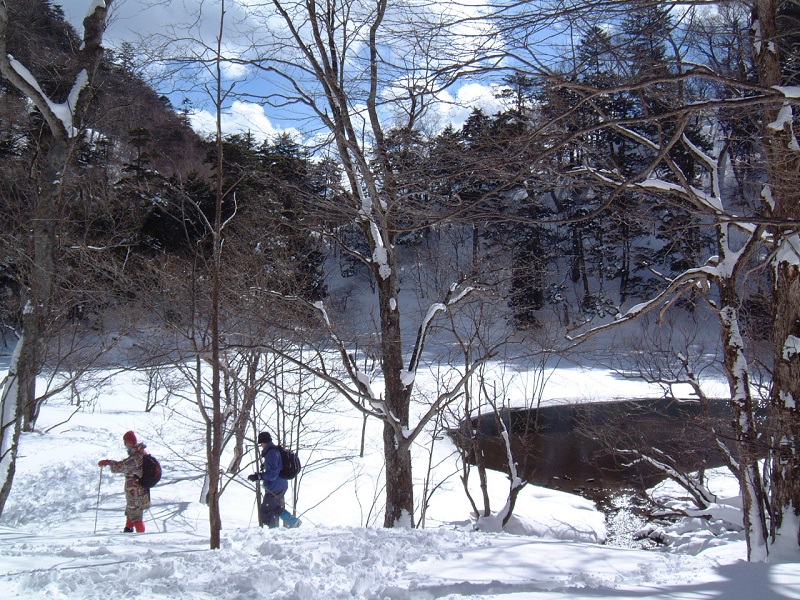 2名の人が湖の横の雪道を歩いているスノーシューツアーの様子を進行方向の横から写した写真