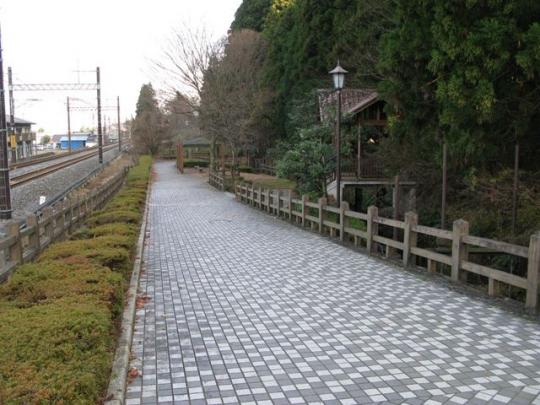 線路わきの道と緑に隠れそうな建物の写真