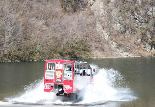 ダックツアーの水陸両用バスが大きな水しぶきをあげて水面に突入する様子の写真