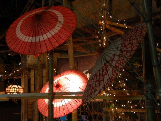 薄暗い竹林の中に和傘が飾られ、ライトアップされている様子の写真
