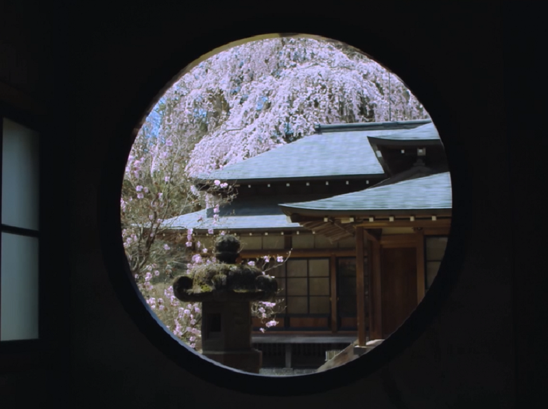 室内の丸い窓から、桜が咲いている日光田母沢御用邸を写した写真