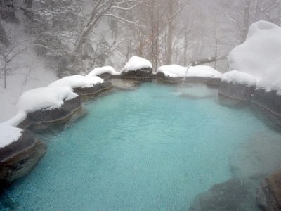 周りが雪化粧をしている中に温泉の湯けむりがみえる手白澤温泉の露天風呂をアップで写した写真