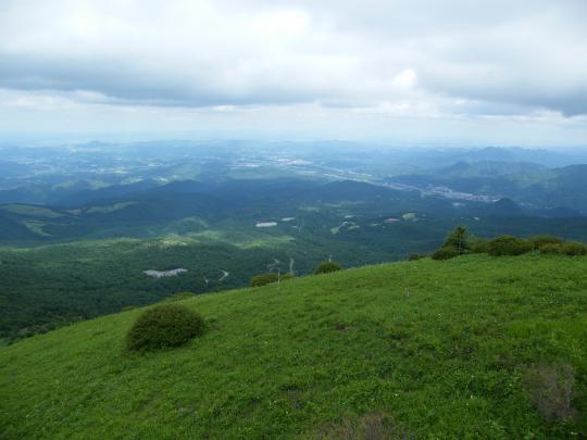 濃淡様々な緑の草木の景色が遠くまで続いており、空の雲が間近に感じるほどの頂上からの眺望写真