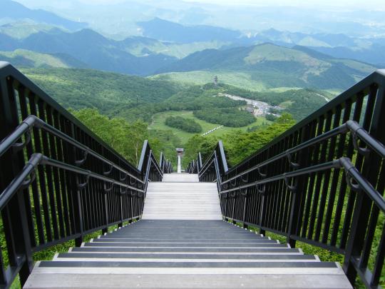 左右両方に手すりがついた下まで続く階段と緑に生い茂った山々を見下ろしている頂上から撮影した写真