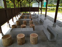 石造りのテーブルに丸太の椅子が6つ並べられているバーベキュー場の写真
