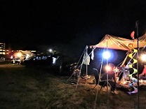 2グループのキャンパー達が、明かりを照らしながらタープの下でバーベキューをしている写真
