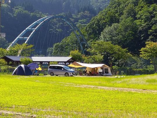 ベージュやネイビーのテントが設置され、シルバーのワゴン車が横付けされている薬師の湯キャンプ場の写真