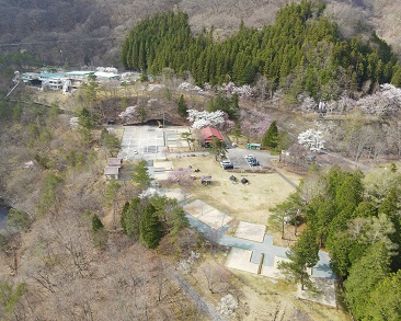 周りを山や木々に囲まれたキャンプ場の様子を上空から撮影した写真