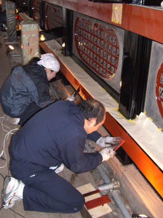 佐藤則武さんと男性が木の部分に茶色の漆塗りをしている様子の写真