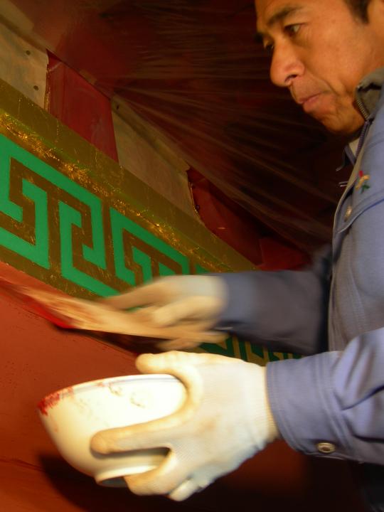 佐藤則武さんが左手に白い器を持ち、刷毛で外壁に漆塗りをしている様子の写真